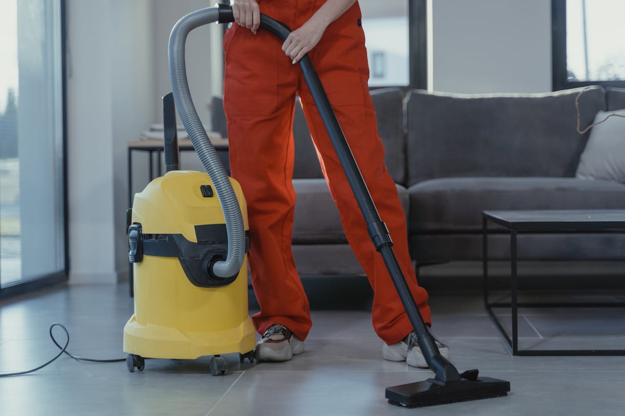 Mastering the First Impression: Your intriguing post title goes here A professional cleaner in red coveralls vacuums a contemporary living room with a yellow vacuum cleaner.